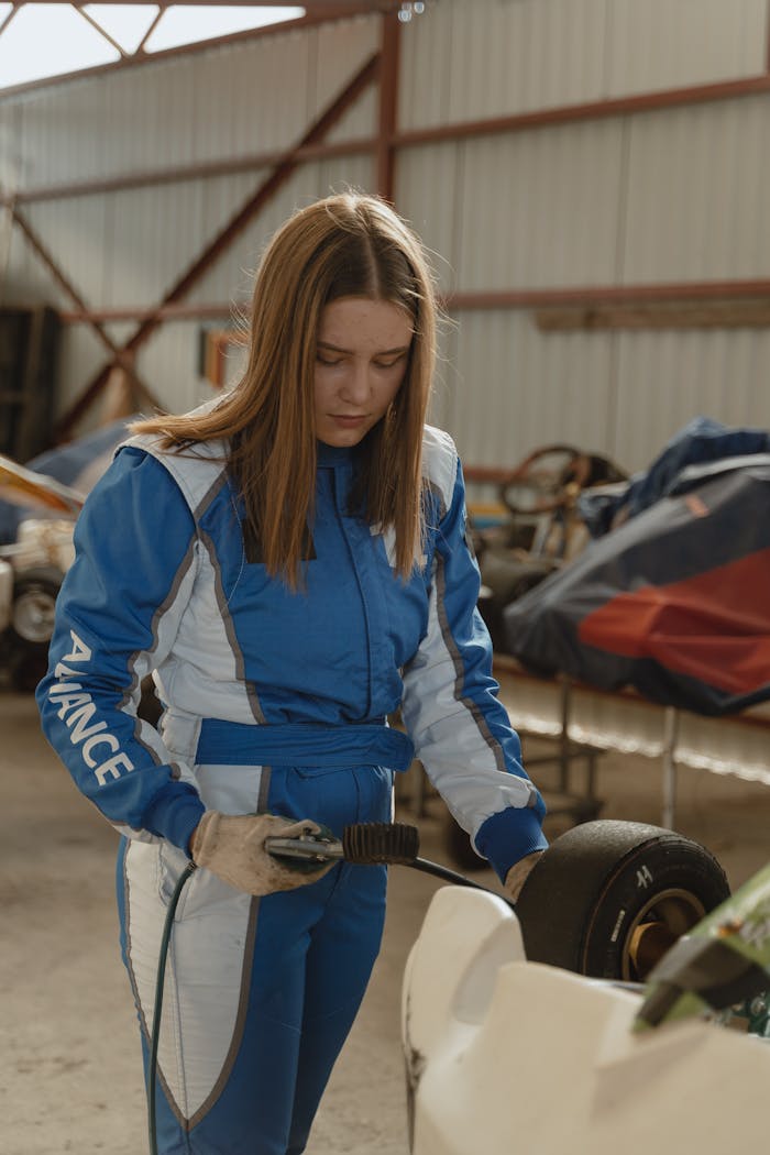 Young female mechanic in a racing suit working on a go-kart in a garage.